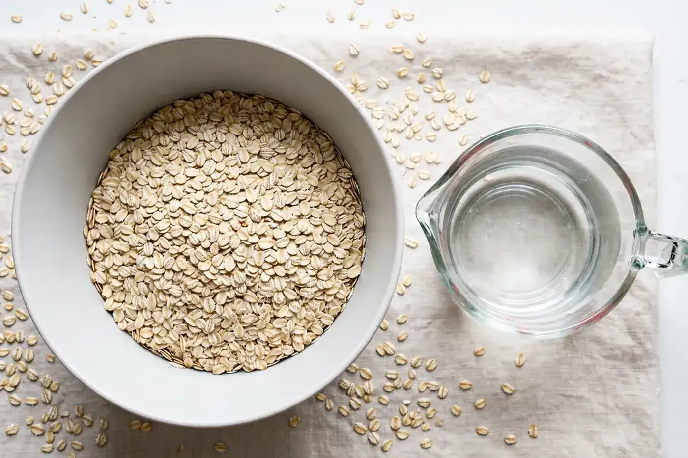 Deep bowl with rolled oats and a glass measuring cup of water from above